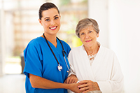 pretty white female caregiver in blue scrubs standing with an elderly white woman in a white robe