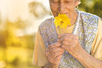 white senior woman smelling a bright yellow flower