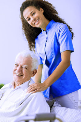 close up of pretty young black female caregiver standing with her hands on the shoulders of an elderly white man sitting in a wheelchair